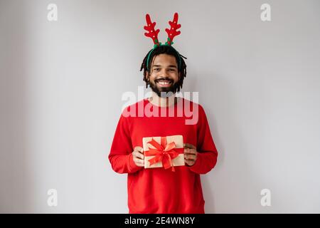 Joyeux afro-américain dans les cornes de cerfs posant avec cadeau boîte isolée sur fond blanc Banque D'Images