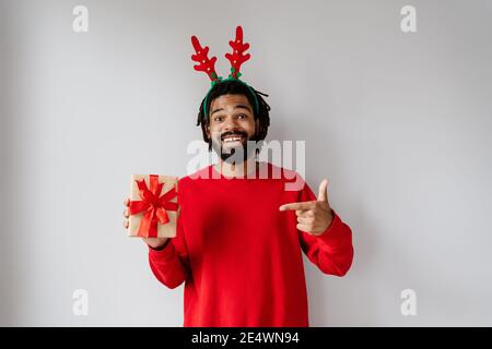 Drôle d'homme afro-américain en tenant et en pointant du doigt vers boîte cadeau isolée sur fond blanc Banque D'Images