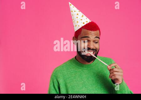 Joyeux afro-américain gars dans le cône de partie faire du plaisir avec chewing-gum isolé sur fond rose Banque D'Images