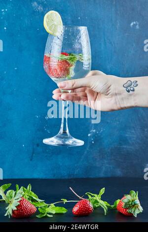 Femme main tenant un verre de jus avec des fruits entiers et menthe à l'intérieur Banque D'Images