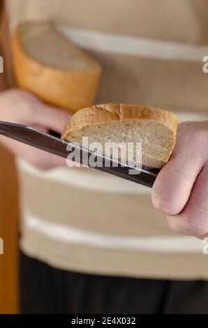 La main d'un homme avec un couteau dans elle retient un pain fraîchement coupé à l'appareil photo. Partager la nourriture, aider ceux qui en ont besoin, concept. Mise au point du point. Banque D'Images