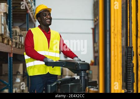 Homme noir travaillant dans un entrepôt avec des boîtes de livraison de chargement de chariot élévateur - concept logistique et industrie Banque D'Images