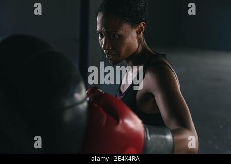 Femme afro-américaine portant des gants de boxe poinçonner le sac de boxe un bâtiment urbain vide Banque D'Images