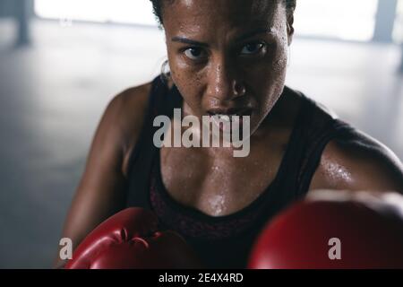 Portrait d'une femme afro-américaine portant des gants de boxe pointant la boxe sac dans un bâtiment urbain vide Banque D'Images