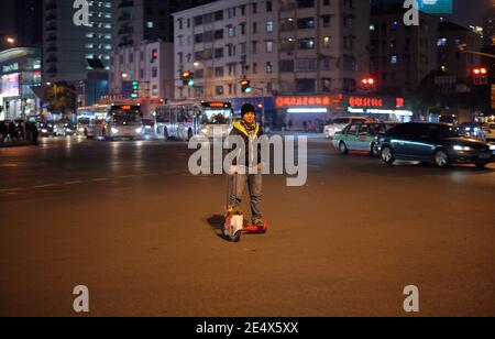 SHANGHAI, CHINE - février 02, 2015 : Young man riding scooter électrique au milieu de la circulation à Shanghai par nuit. Carrefour, T Banque D'Images