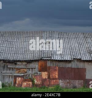 Ancienne ferme en bois vieillie, en bois plaqué gris, panneau mural de cabane, planches plaquées, plaques de métal rouillées, texture de peinture rouillée, ciel nuageux Banque D'Images