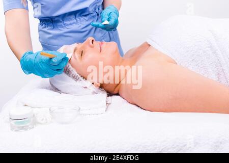 Photo agrandie. L'esthéticienne applique un masque hydratant au visage d'une femme plus âgée avec une brosse. Banque D'Images