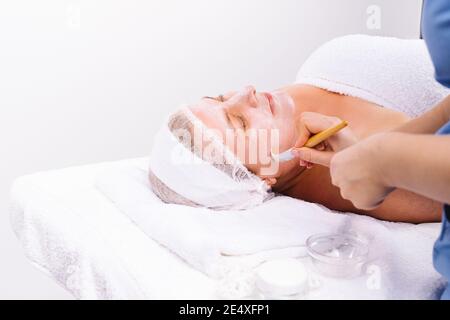 Photo agrandie. L'esthéticienne applique un masque hydratant au visage d'une femme plus âgée avec une brosse. Banque D'Images