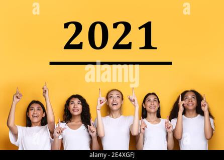 Multiculturel Dames pointant des doigts au numéro 2021 au-dessus de la tête, fond jaune Banque D'Images