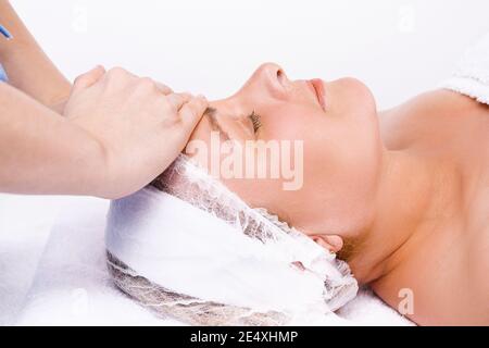 Photo agrandie. Les mains du maître massent le visage d'une femme plus âgée. Arrière-plan blanc. Banque D'Images