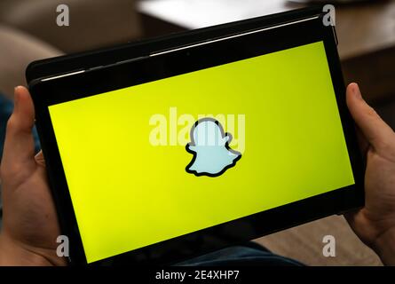 Mains tenant la tablette avec le logo jaune Snapchat sur un écran noir. Banque D'Images