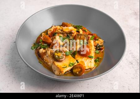 Poisson sicilien traditionnel avec tomates, olives, persil et poivre rouge dans une assiette profonde sur fond clair, gros plan Banque D'Images