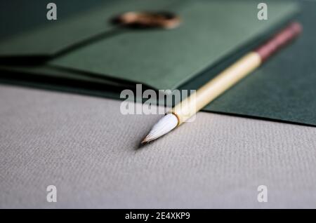 Gros plan de papier beaux-arts de couleur verte, une enveloppe verte avec un sceau doré et une brosse de calligraphie en bois posée dessus Banque D'Images