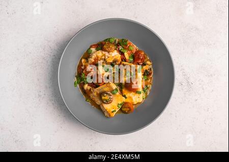 Poisson sicilien traditionnel avec tomates, olives, persil et poivre rouge dans une assiette profonde sur fond clair, vue du dessus Banque D'Images