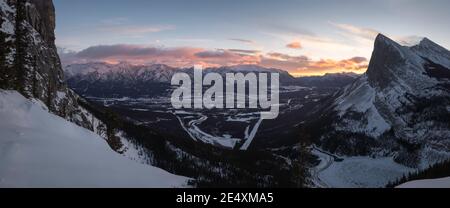 Vue panoramique sur le lever du soleil depuis l'extrémité est du mont Rundle, surplombant la ville de Canmore et le pic de Ha Ling à travers le creux de la vallée. Banque D'Images