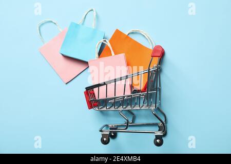Panier à provisions rempli de sacs en papier colorés sur bleu clair, un panier à provisions, un concept de vente joyeuse et de vente au détail Banque D'Images