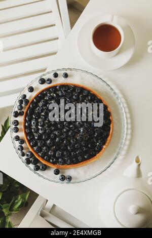 Petit-déjeuner vertical avec une tarte aux myrtilles et une tasse de thé, un matin calme de tarte aux myrtilles et de thé chaud sur une table blanche Banque D'Images