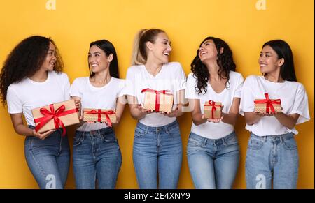 Des dames joyeuses posant avec des cadeaux célébrant les fêtes sur fond jaune Banque D'Images