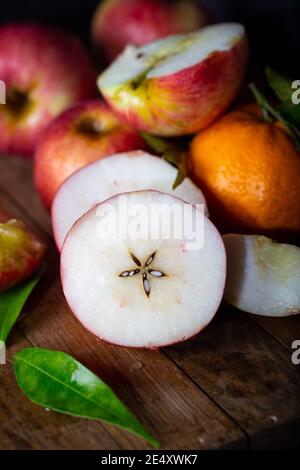 Des pommes rouges fraîches, entières et en moitiés, placées sur un parquet rustique. Banque D'Images