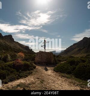 PORT DE POLLENCA, PORTUGAL - 06 mars 2020: Homme faisant du yoga sur un rocher dans une vallée avec le soleil sur lui Banque D'Images