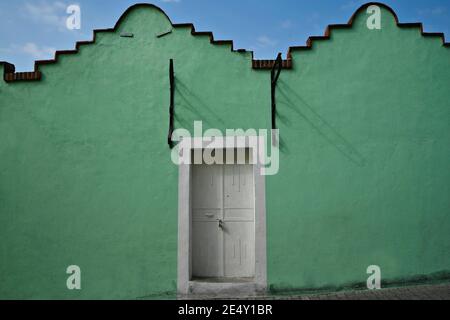 Façade de maison en Adobe avec un mur en stuc vert turquoise et une porte en bois blanc à Atlixco, Puebla Mexico. Banque D'Images