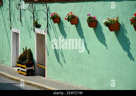 Façade de maison en Adobe avec un mur en stuc vert turquoise, une porte en fer et des pots en argile faits à la main avec des géraniums à Atlixco, Puebla Mexique. Banque D'Images