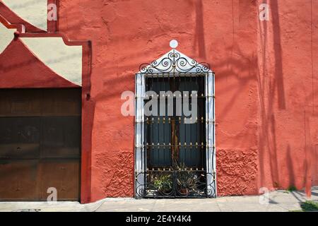 Ancienne façade de maison coloniale avec un mur en stuc rouge vénitien et une fenêtre avec garniture blanche et grilles en fer artisanales à Atlixco, Puebla Mexique. Banque D'Images