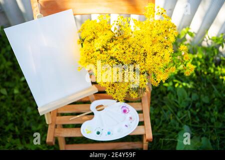 Une palette de peintures multicolores aquarelle se dresse sur une chaise en bois et un bouquet de fleurs jaunes, un passe-temps créatif, dessinant dans la rue Banque D'Images