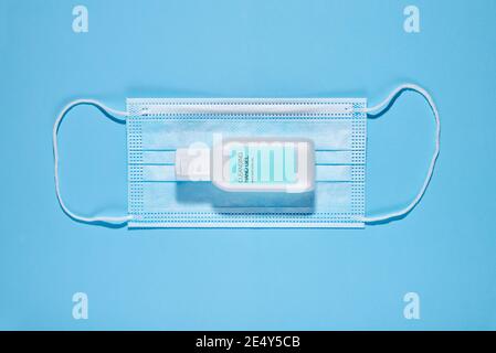 Du dessus du masque de protection propre avec une bouteille de gel désinfectant pour les mains composé sur fond bleu Banque D'Images