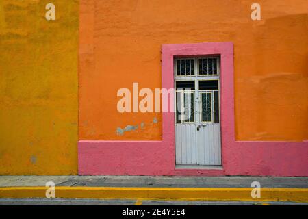 Ancienne façade de maison coloniale avec un mur en stuc orange vénitien coloré, rose et ocre et une porte d'entrée en fer blanc à Atlixco, Puebla Mexico. Banque D'Images