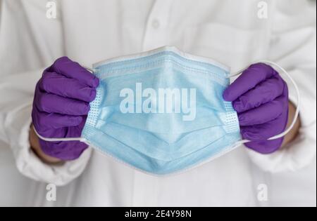 Masque chirurgical tenu par un médecin avec des gants. Masque médical de protection bleu pour arrêter la propagation des virus et des germes Banque D'Images