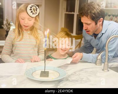 père et enfants éclairant ensemble la menorah d'hanoukkah Banque D'Images