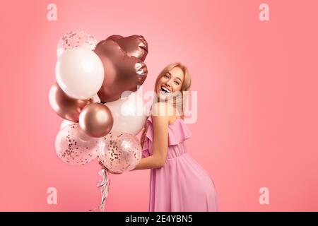Une jeune femme insouciante avec des ballons de vacances festifs, célébrant anniversaire ou anniversaire sur fond rose studio Banque D'Images