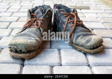 Une paire de bottes sales. Vieilles chaussures en cuir bleu foncé avec lacets marron variables. Arrière-plan des finisseurs gris. Le concept de pauvreté, sans-abri Banque D'Images