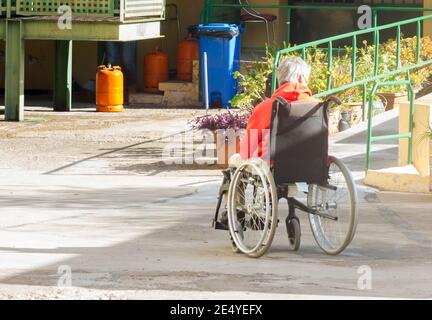 VALENCE, ESPAGNE - 15 janvier 2021 : un vieux solitaire en fauteuil roulant profite des rayons du soleil de la rue pour se réchauffer en hiver Banque D'Images
