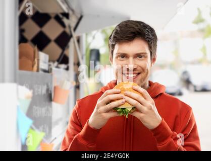 un jeune homme heureux mangeant un hamburger dans un camion Banque D'Images