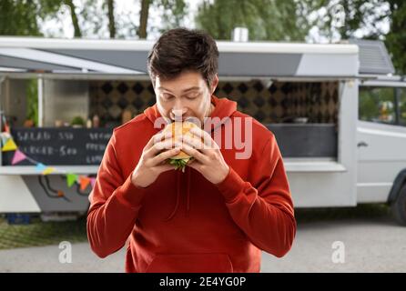 un jeune homme affamé mangeant un hamburger dans un camion alimentaire Banque D'Images