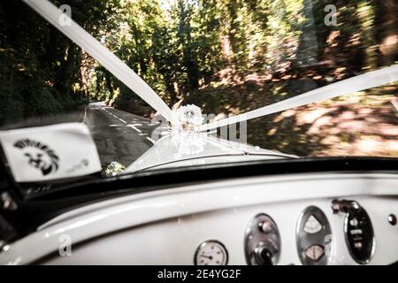 Une voiture de mariage avec des rubans qui empruntant la campagne à grande vitesse ruban blanc classique de l'intérieur de véhicule ancien vue à travers le pare-brise avant dans la crème de luxe Banque D'Images