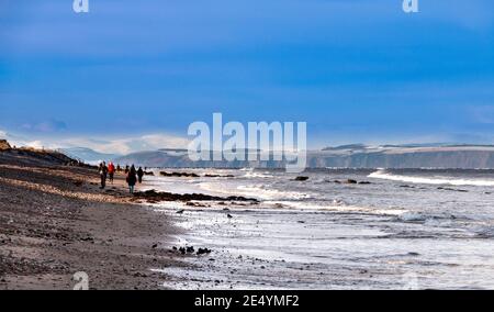 MORAY COAST SCOTLAND WINTER BEACH SCENE AVEC RANDONNEURS AHD JOGGEURS NEIGE SUR LES MONTAGNES DE L'ÎLE NOIRE AU LOIN Banque D'Images