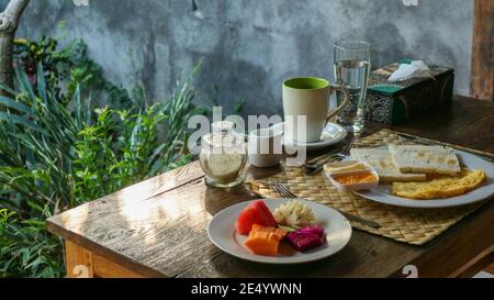 Petit déjeuner touristique traditionnel à Bali : pain grillé, œufs brouillés, café et fruits frais Banque D'Images