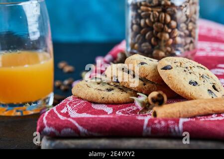 Biscuits aux pépites de chocolat, grains de café dans un pot en verre et un verre de jus d'orange sur table sombre Banque D'Images