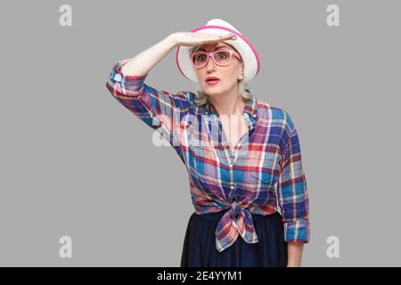 À la recherche de quelque chose jusqu'à présent. Portrait de femme mature élégant moderne attentif au style décontracté avec chapeau et lunettes debout avec la main sur le front Banque D'Images