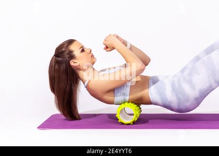 Portrait de profil femme sportive allongé sur un tapis de yoga à l'aide d'un masseur à roulettes en mousse sur le haut du dos pour la détente, l'étirement des muscles de la colonne vertébrale, l'entraînement. Po Banque D'Images