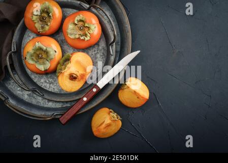 Fruits Persimmons mûrs frais biologiques sur plateau métallique avec tranche sur fond noir, vue de dessus Banque D'Images