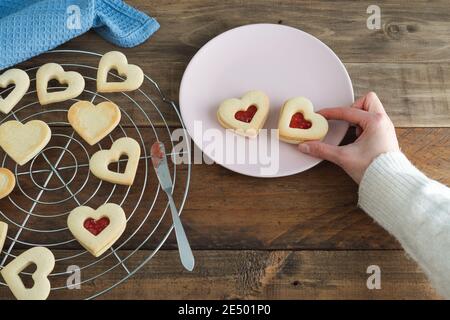 Main de femme plaçant des biscuits en forme de coeur sur l'assiette. Copier l'espace. Concept de la Saint-Valentin. Banque D'Images