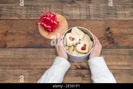 Les mains des femmes avec une boîte ouverte de biscuits en forme de coeur sur une base en bois. Concept Saint-Valentin, Fête des mères, anniversaire. Banque D'Images