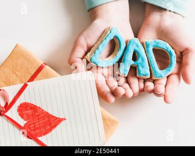 Les mains de l'enfant et l'adulte man's hands, superbe boîte cadeau, ruban et enrobée de cookies sur un fond de bois, blanc. Vue de dessus, close-up. La préparation pour le th Banque D'Images