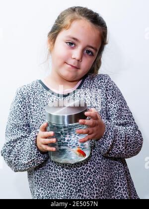 Photo verticale d'une petite fille caucasienne tenant un pot avec un poisson orange à l'intérieur Banque D'Images