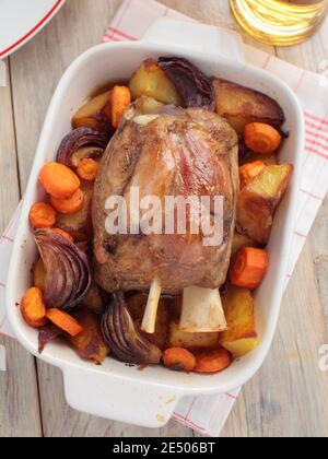 Le plat traditionnel allemand Eisbein, porte-jarret de porc rôti avec pommes de terre grillées, carottes et oignons sur une table rustique Banque D'Images