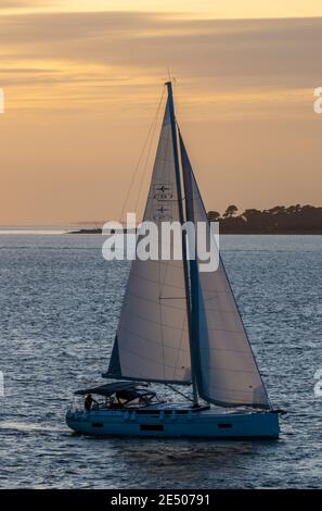 grand yacht à voile ou bateau revenant au port au coucher du soleil en semi-silhouette. Banque D'Images